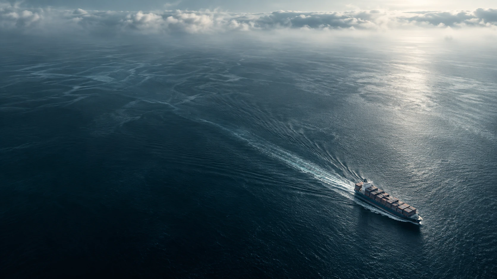 Extreme high drone vista of a container ship tracing a fine diagonal white wake through vast almost abstract teal-black water, tiny vessel at lower right, elegantly immense scale.