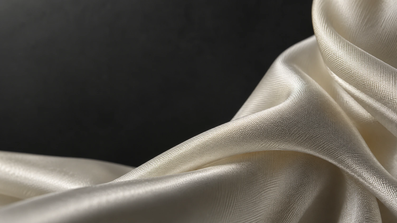 Macro of folded ivory silk sweeping in from the lower left, delicate woven threads and soft sculptural shadows, charcoal backdrop.