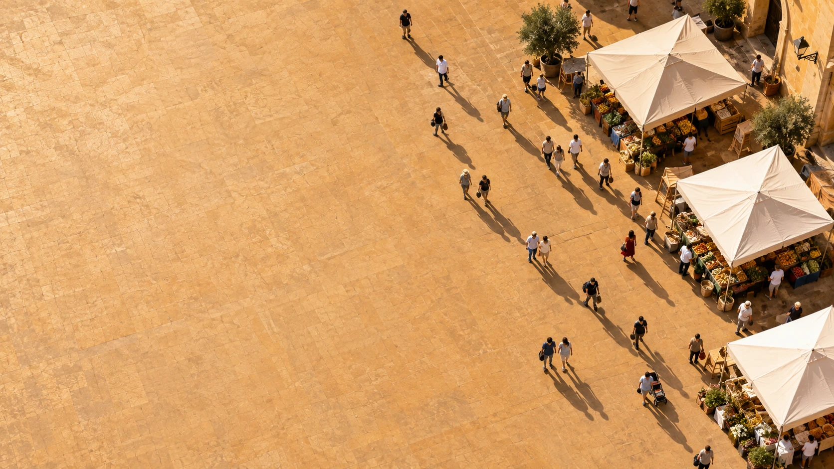 Aerial view of tiny people navigating a few simple unbranded canvas market canopies clustered along the right of an open ochre plaza.