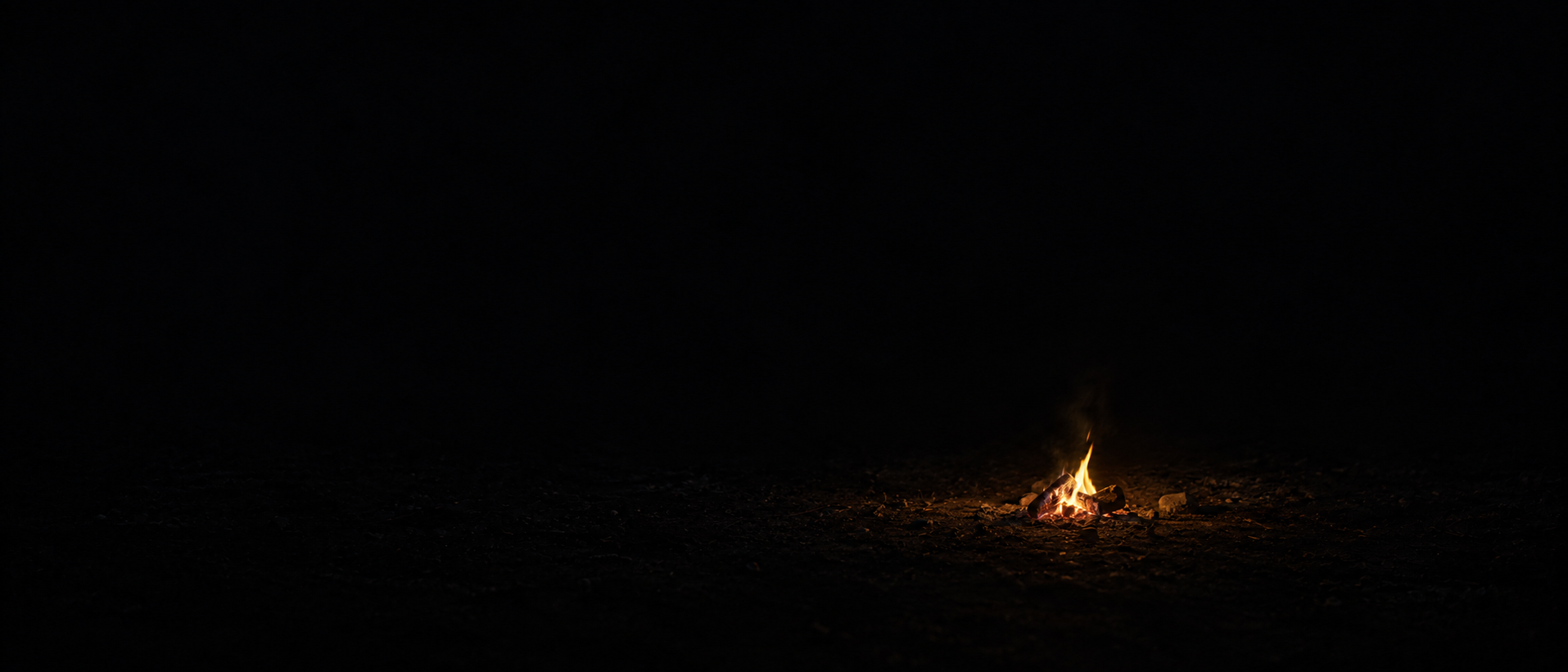 A small irregular campfire burns on dark earth, with broad black space above and to the left.