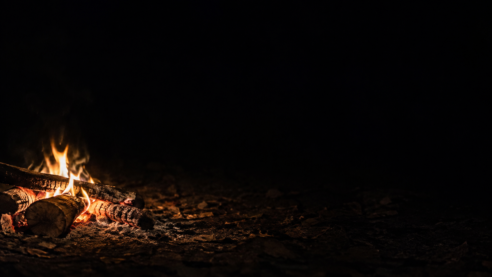 A low campfire on the far left illuminates a small patch of rough earth.