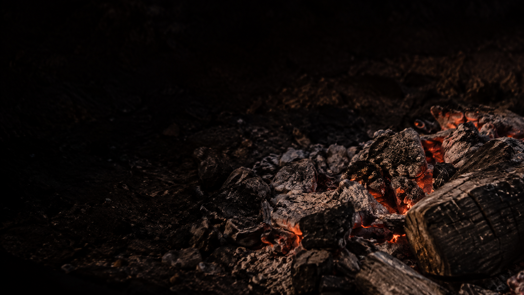 Gray ash and broken charcoal reveal a few deep orange fissures in the lower right.