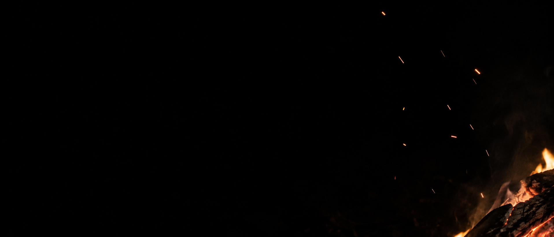 A few uneven amber sparks rise above a cropped campfire at the lower right.
