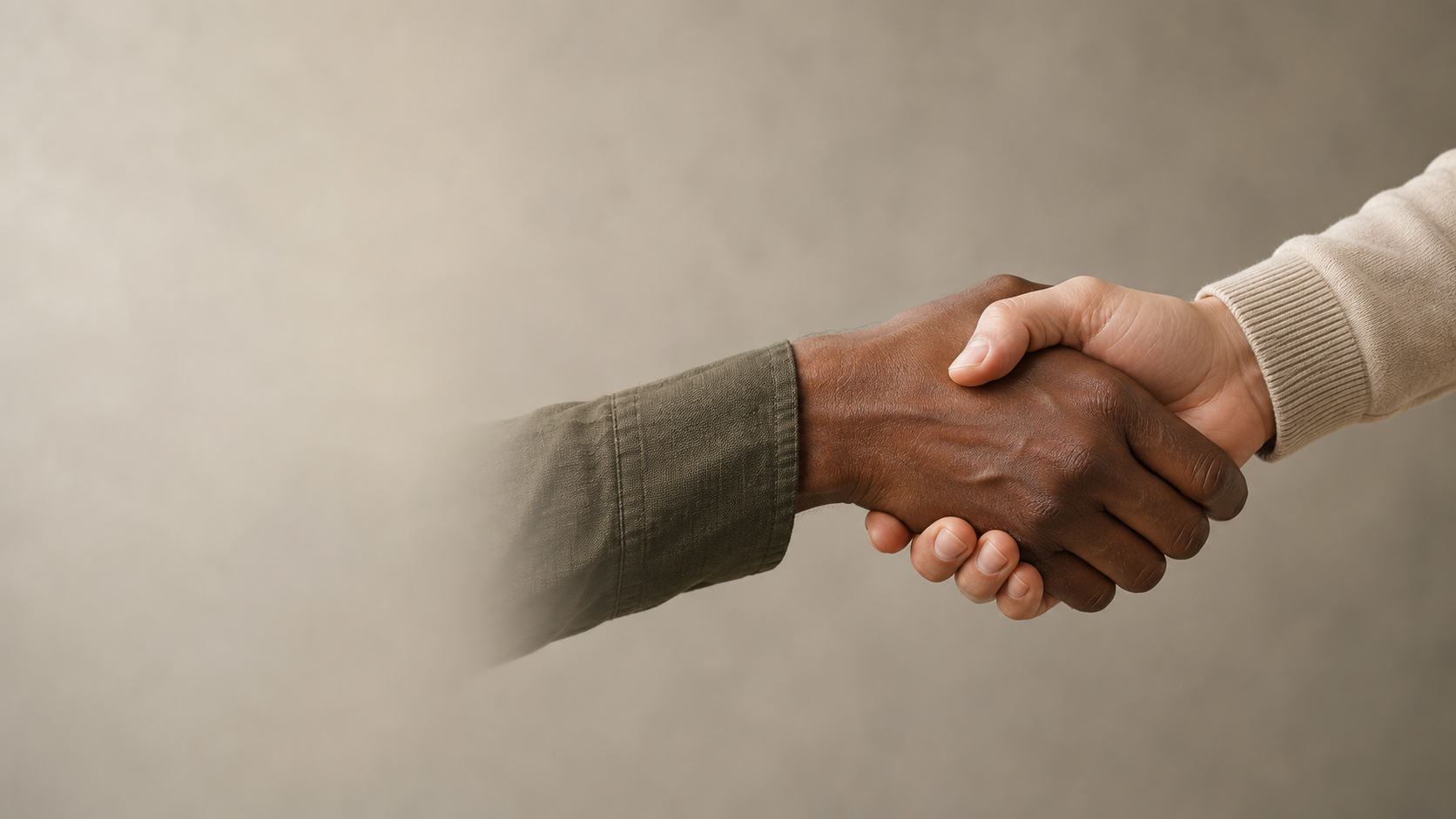 Close-up of exactly two adults exchanging a natural handshake on the right of a softly lit warm-gray studio backdrop; one dark-skinned and one light-skinned hand, sleeves simple and unbranded.