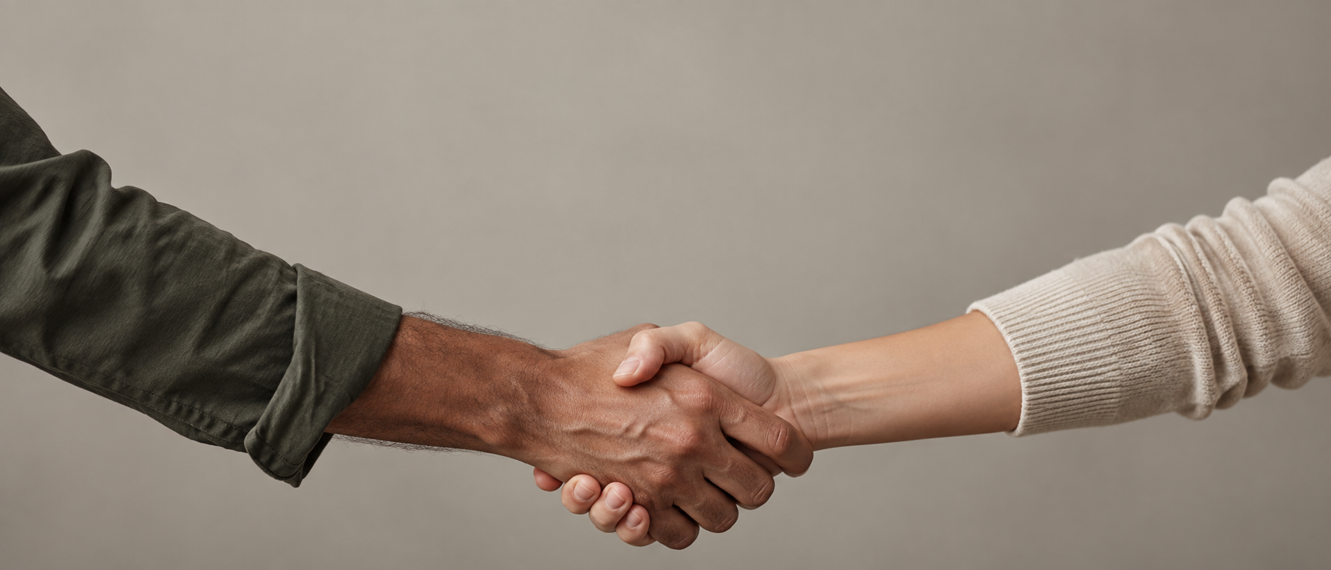 A wide panoramic editorial image of two adult forearms reaching from opposite edges to meet in one anatomically correct handshake low in the frame, plain warm gray backdrop.