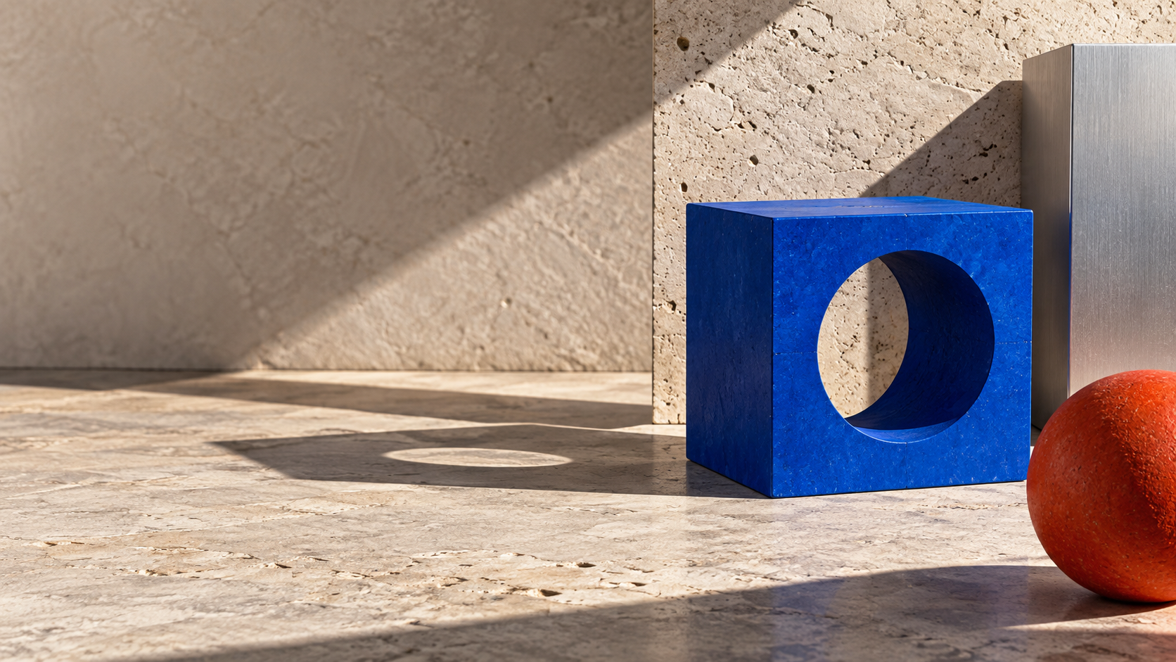 A bright cobalt cube with one circular cutout casts a long hard shadow on warm gray stone.