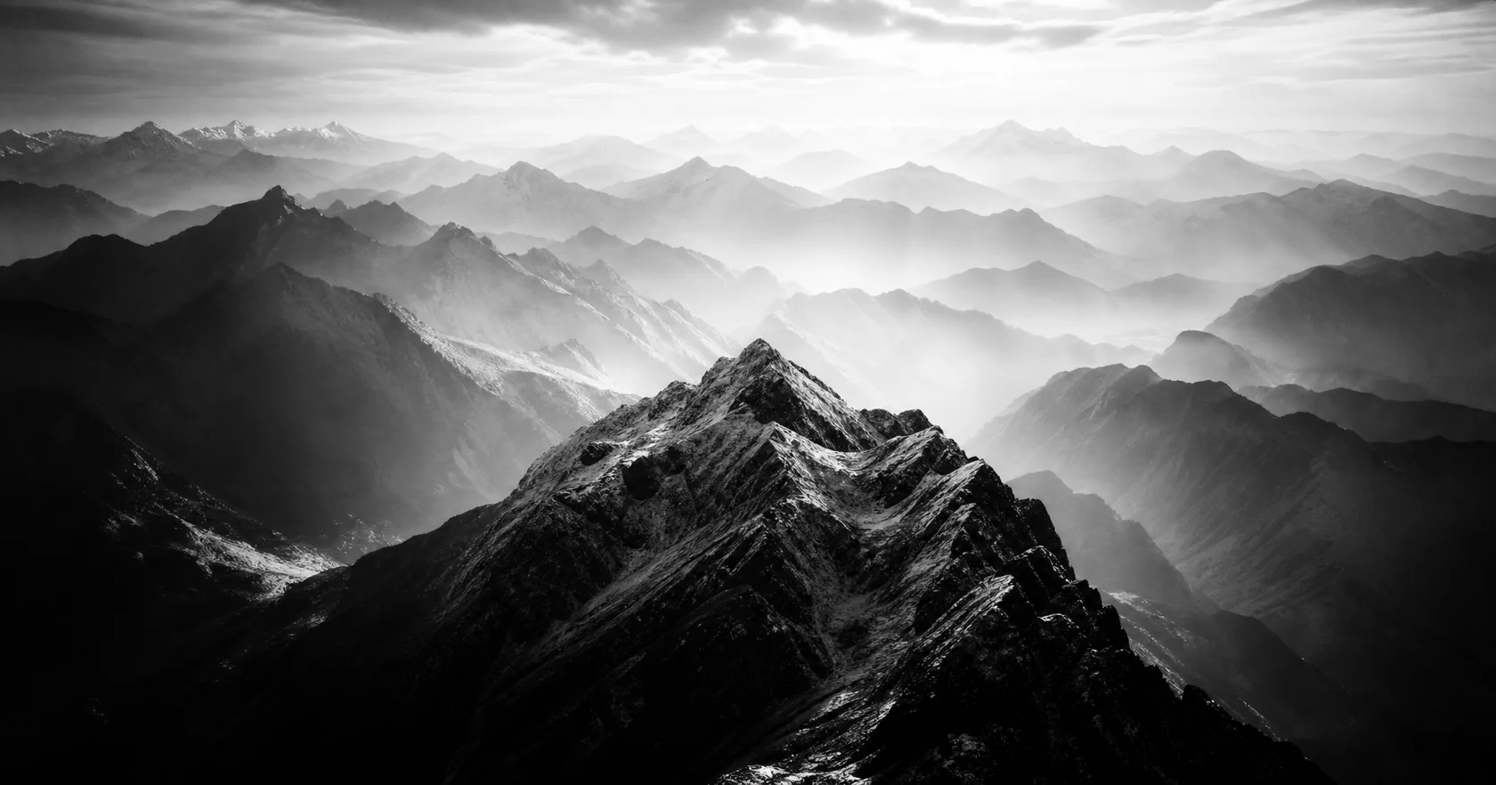An aerial panorama of distant alpine ranges in cool evening shadows.