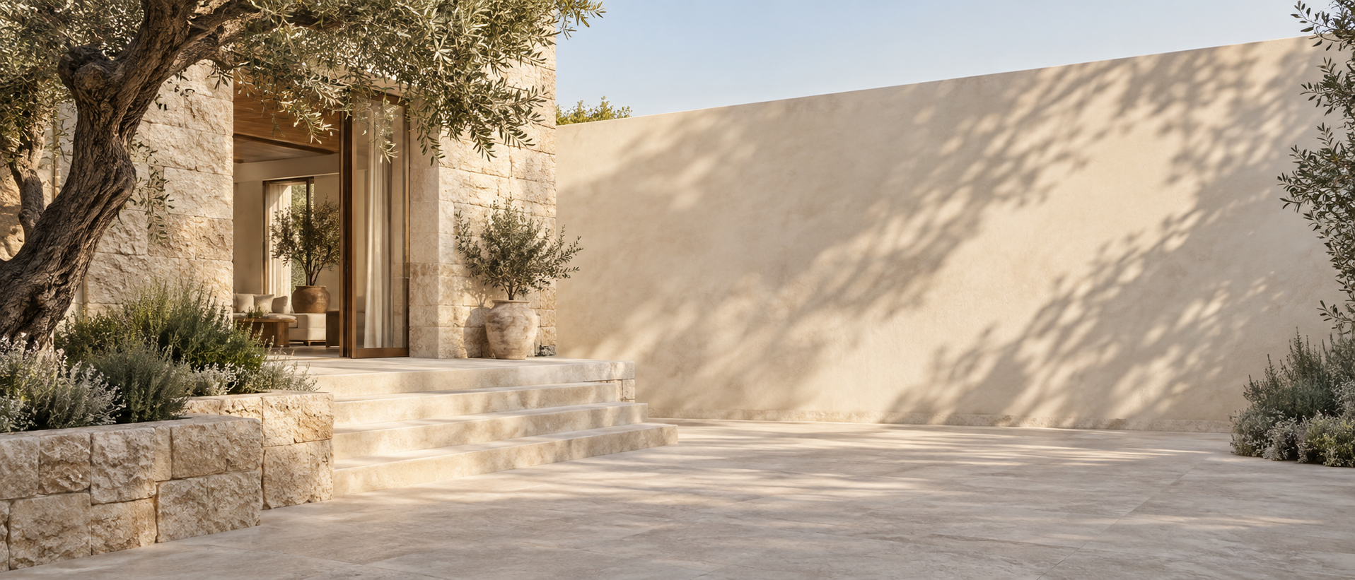 Restrained limestone villa on LEFT with olive tree and pale steps, right 60 percent open sunlit courtyard wall fading into soft shadows.
