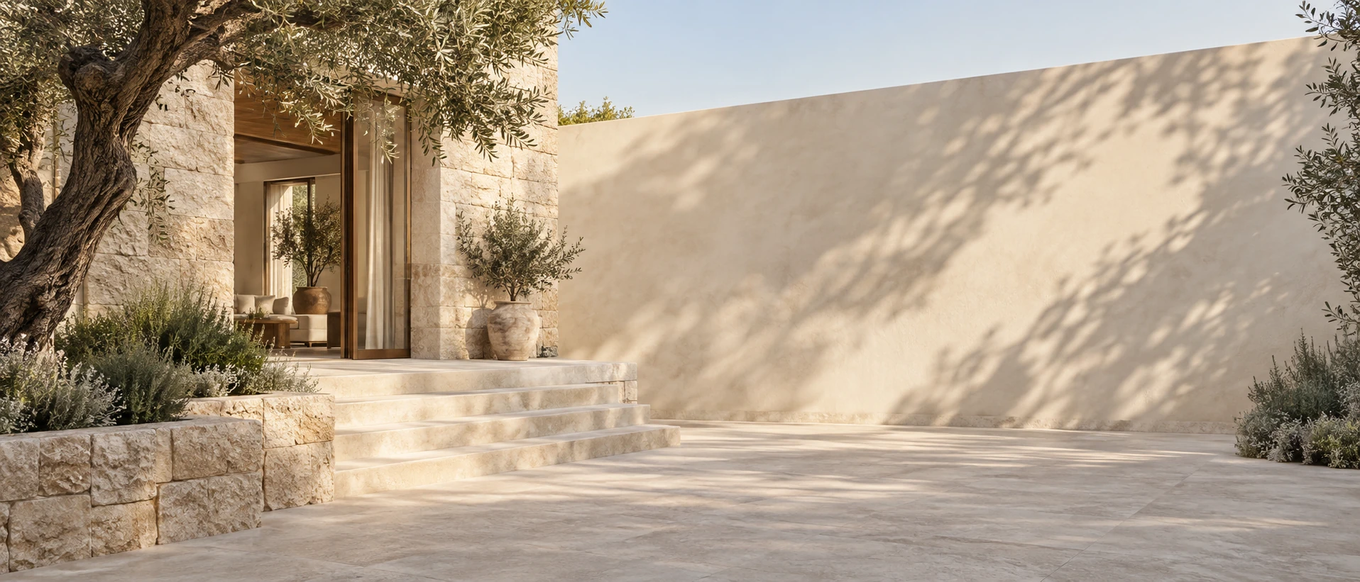 Restrained limestone villa on LEFT with olive tree and pale steps, right 60 percent open sunlit courtyard wall fading into soft shadows.