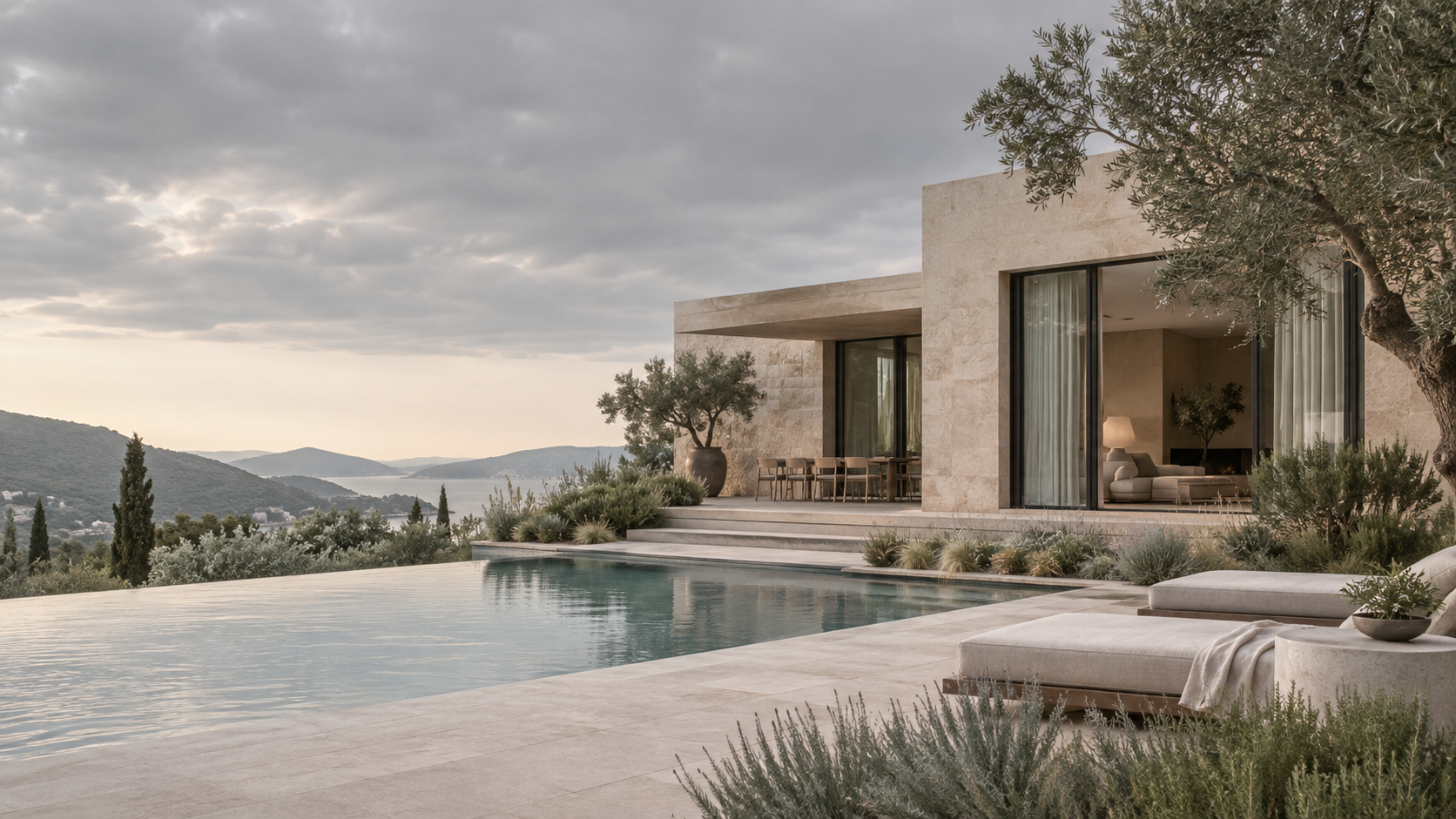 Modern residence in pale blush limestone beneath overcast sky, garden beds with soft grasses, sage-green glazing reflections, serene distinctive cooler color treatment.